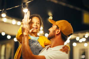 Dad holding young daughter as they high-five.